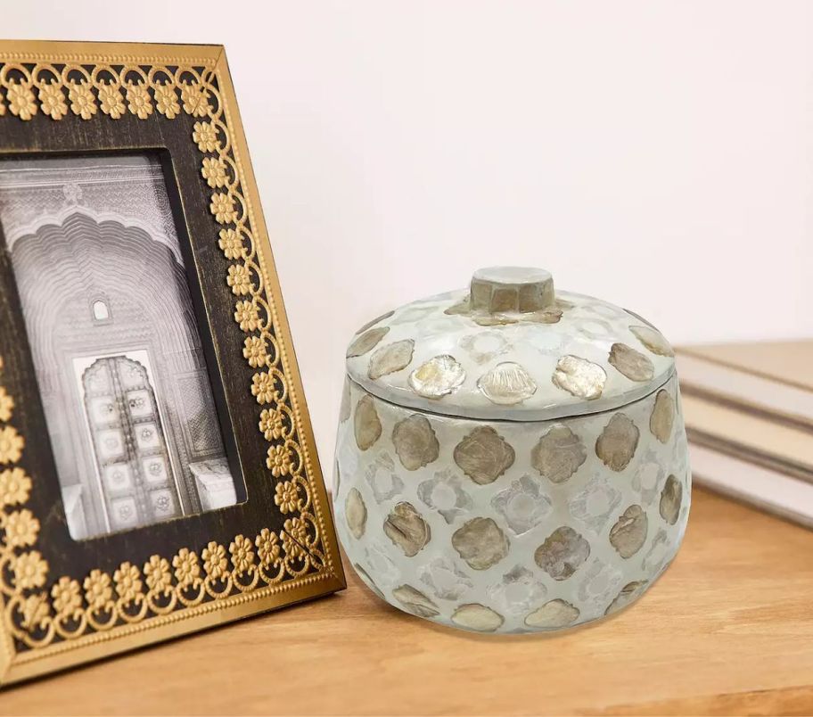 a small round lidded trinket box next to a gold picture frame