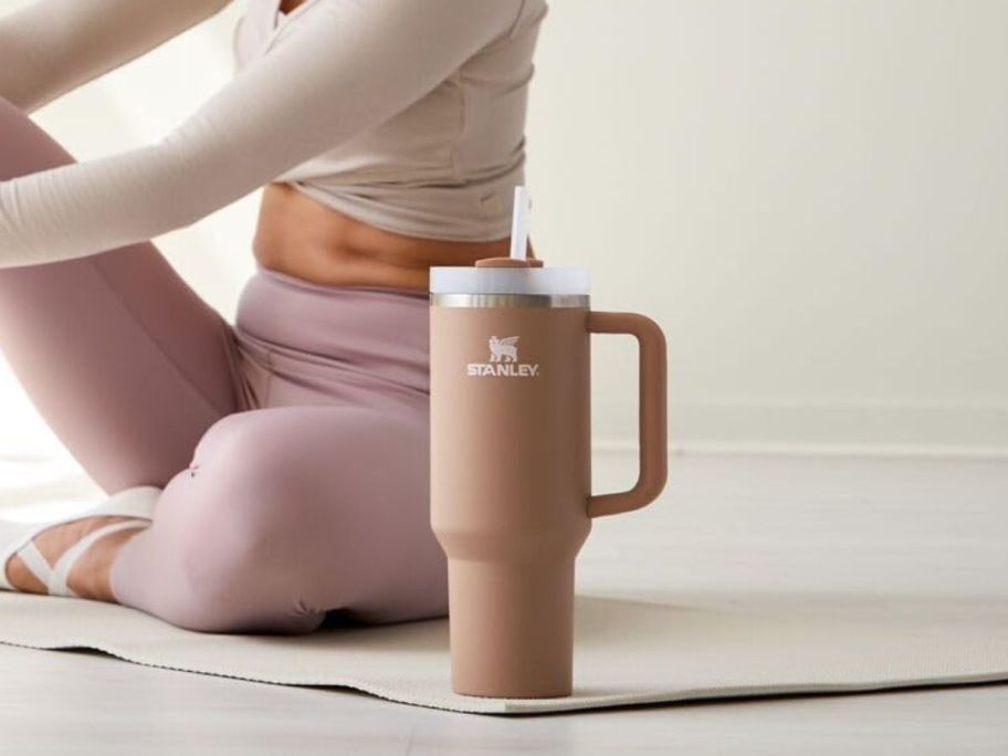 A woman on a yoga mat with a Stanley in Almond Rose