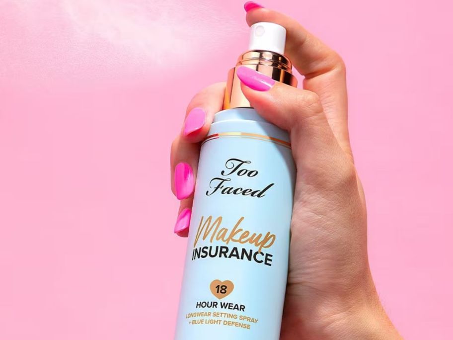 Hand spraying a bottle of Too Faced Makeup Insurance Longwear Setting Spray + Blue Light Defense 