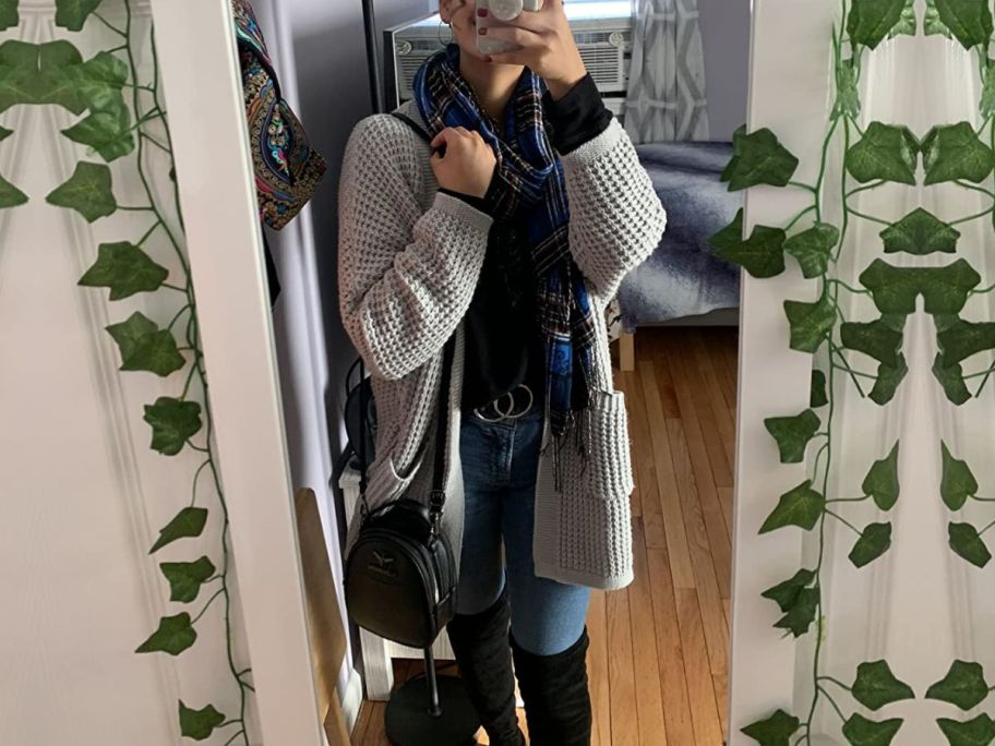 Woman in a mirror wearing a Zesica cardigan sweater with a top, jeans, purse and tall boots