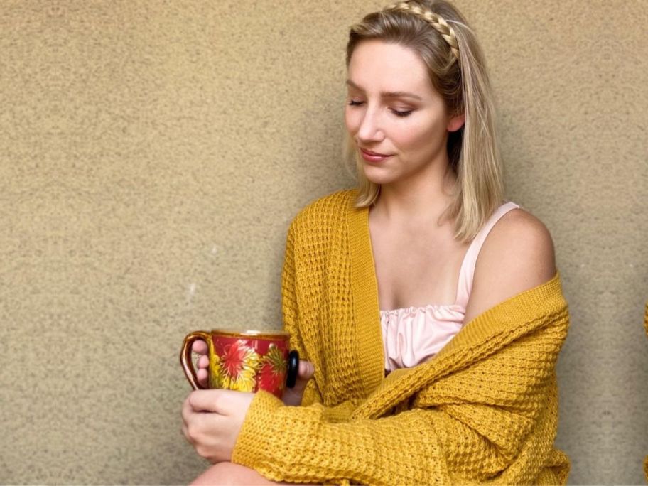 woman sitting drinking a cup of coffee wearing a cardigan sweater