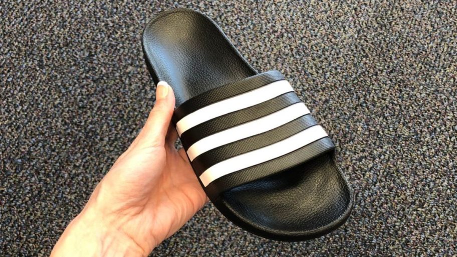 a womans hand holding an adidas slide shoe