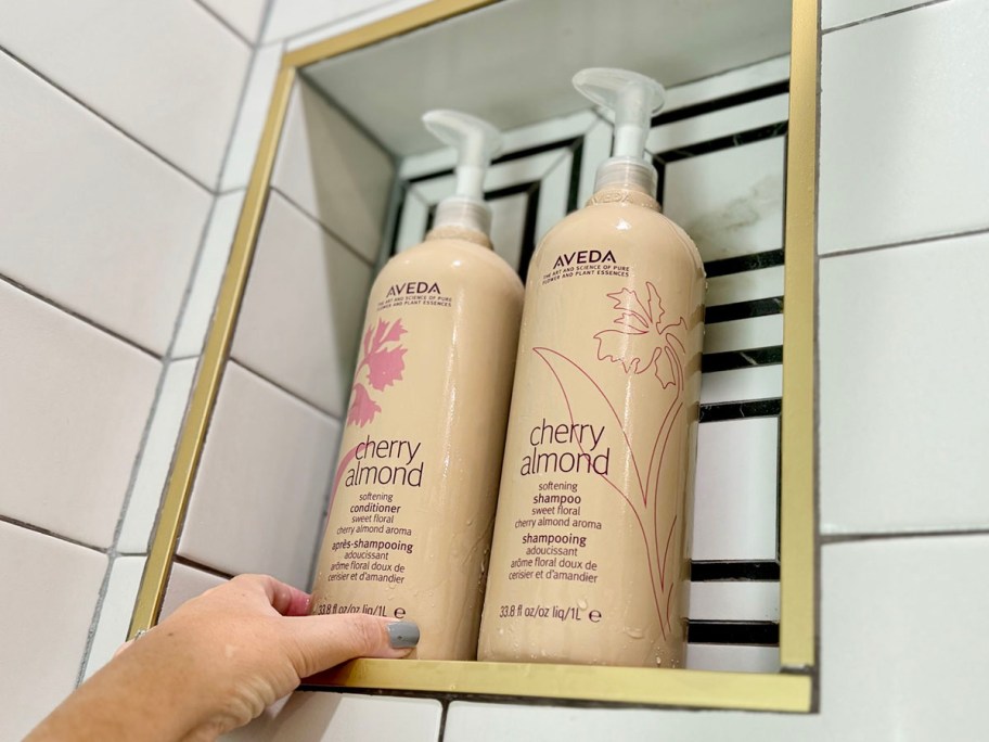 hand reaching for aveda shampoo and conditioner bottle in shower