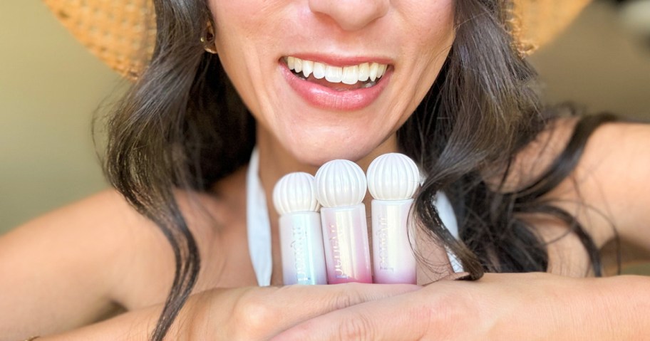 smiling woman wearing a straw hat holding up 3 benefit lip tints