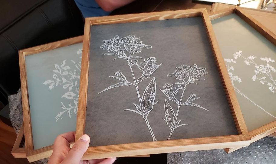 a womans hand holding the corner of a framed art print