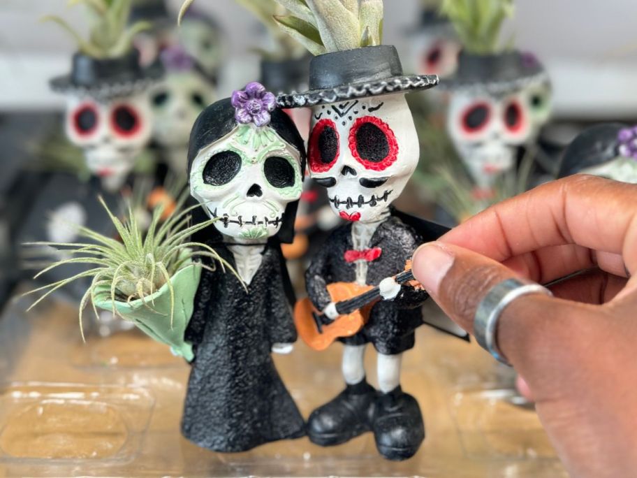 a womans hand holding 2 dia de los Muertos woman and man planters with succulents