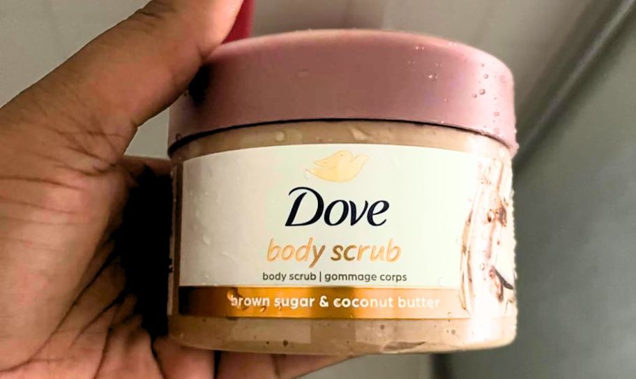 a womans hand holding a jar of dove body scrub