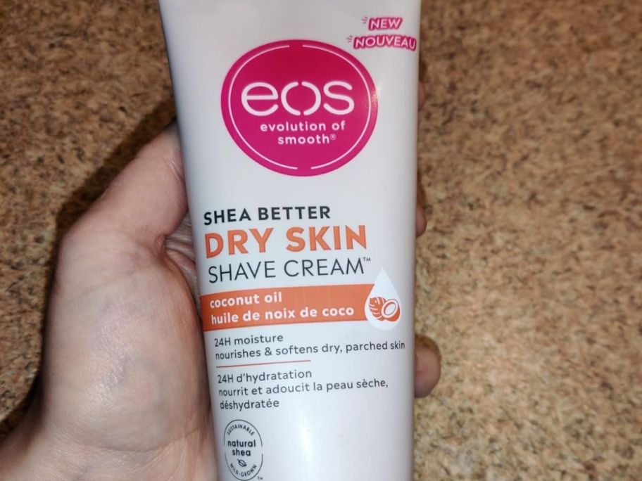 A person holding a tube of eos Shea Shave Cream