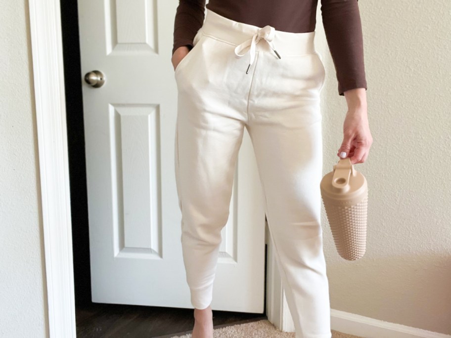 woman in white joggers holding water bottle