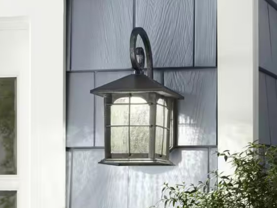 black metal lantern style outdoor wall light on a blue shingle wall next to a window