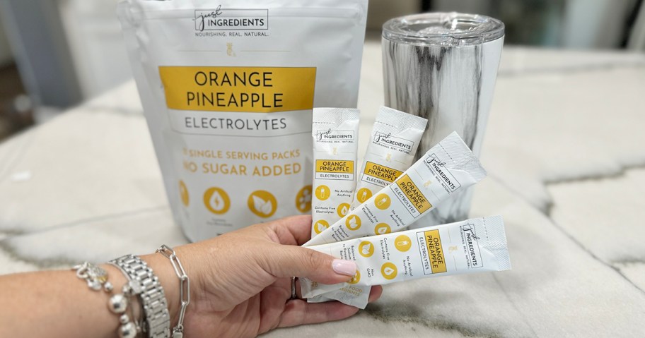 hand holding orange pineapple packets with bag and cup behind it on counter