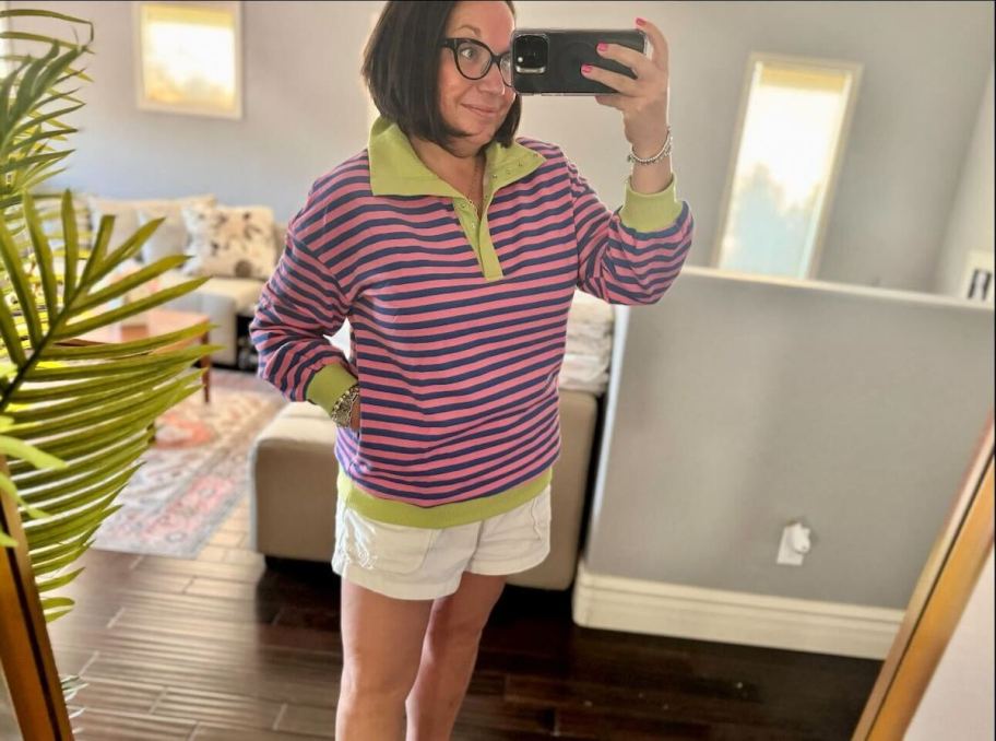 woman taking selfie in mirror wearing striped pullover and white shorts