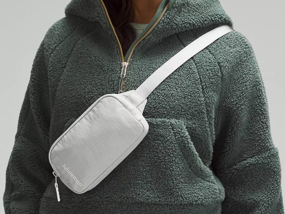 woman in a green sherpa hoodie with a light grey belt bag