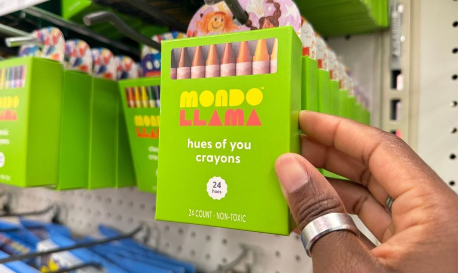 a womans hand grabbing a pack of crayons off a peg in a store