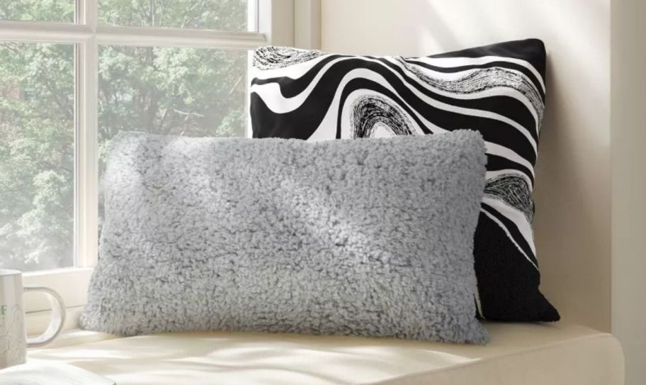 a black and white swirl pillow shown with a faux fur lumbar pillow on a window seat