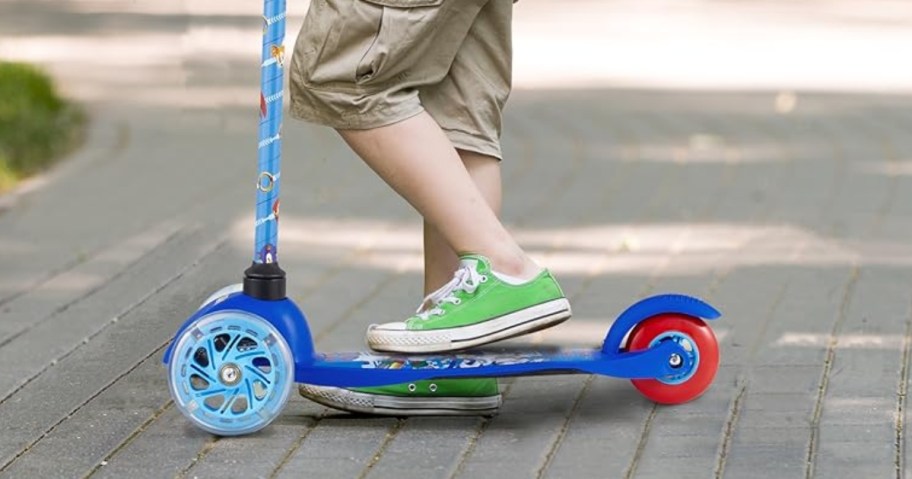 little boy with green sneakers riding a blue and red Sonic scooter