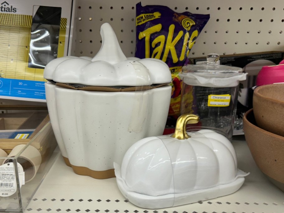 a cream color serving dish with lid shaped like a pumpkin and a cream and gold butter dish shaped like a pumpkin on a store shelf