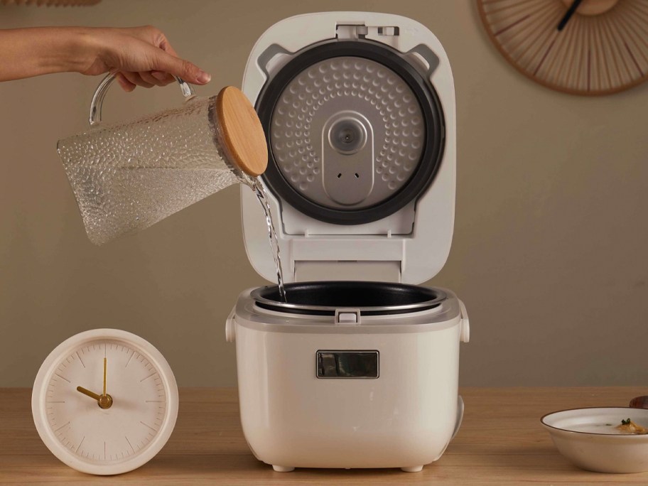 someone pouring water into white toshiba rice cooker 