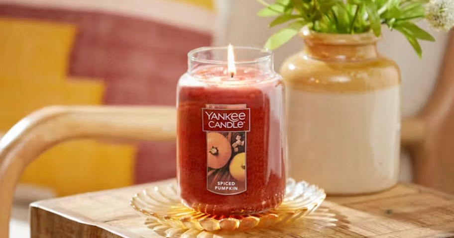 yankee candle pumpkin spice candle on table next to vase with flowers