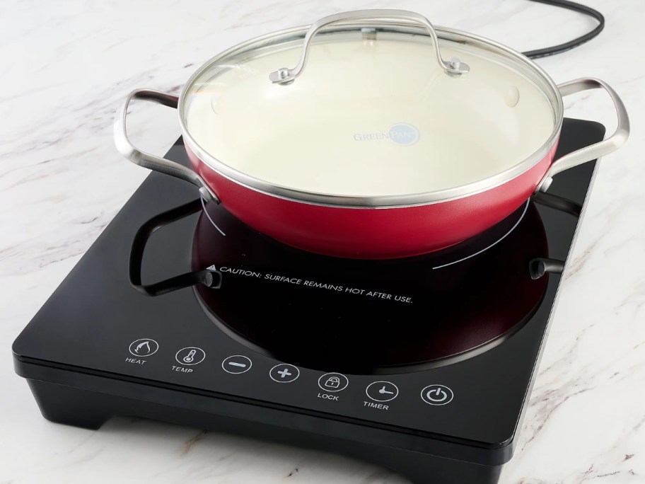 induction burner with a red pan with a glass lid on top