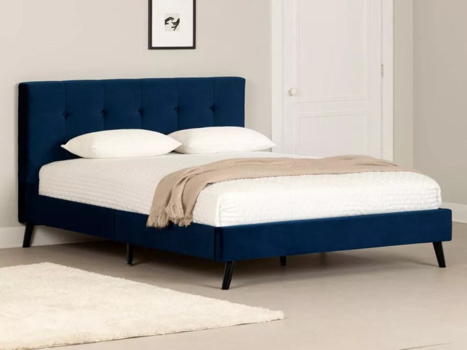 navy blue upholstered bed frame with a mattress and pillows on it in a bedroom