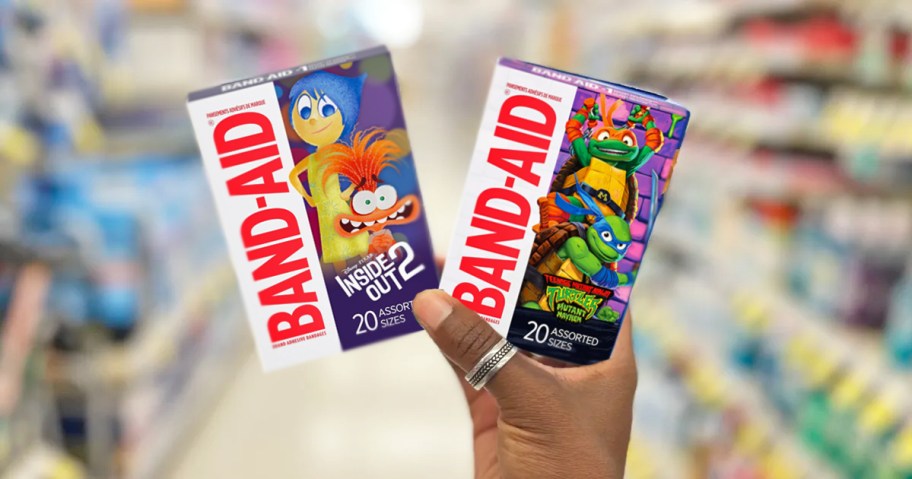 hand holding up two boxes of Band-Aid Bandages in Inside Out and TMNT prints