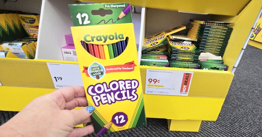 hand holding up a pack of crayola colored pencils in front of sale sign