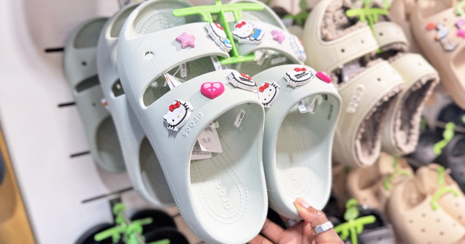 hand touching a pair of white crocs sandals with hello kitty charms