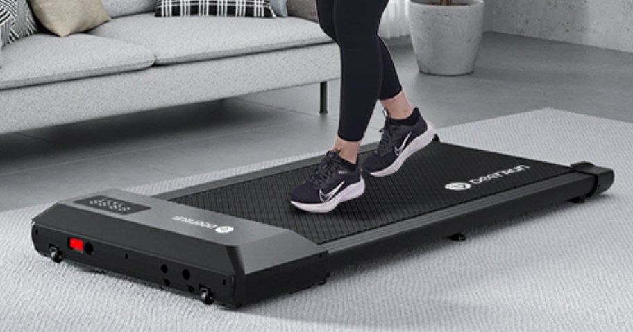 woman's legs and feet wearing black tennis shoes walking on a black walking pad in a living room