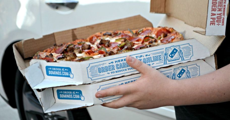 Hands carrying two large Domino's pizza boxes