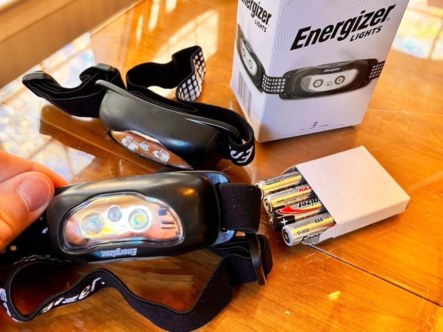 hand holding an Energizer LED Headlamp with another and pack of batteries in background