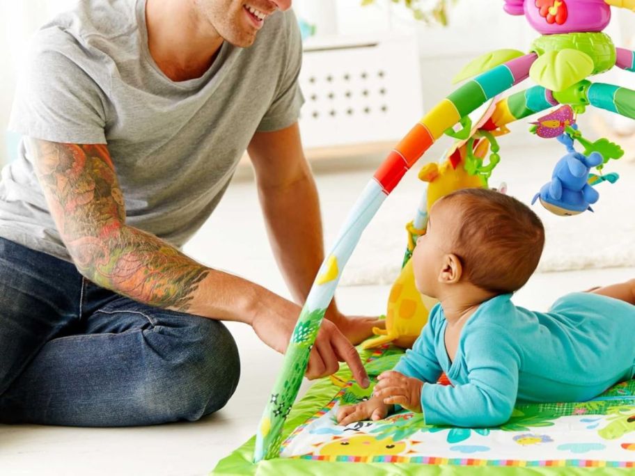 baby on Fisher-Price Rainforest Music & Lights Deluxe Baby Gym Play Mat with man next to it