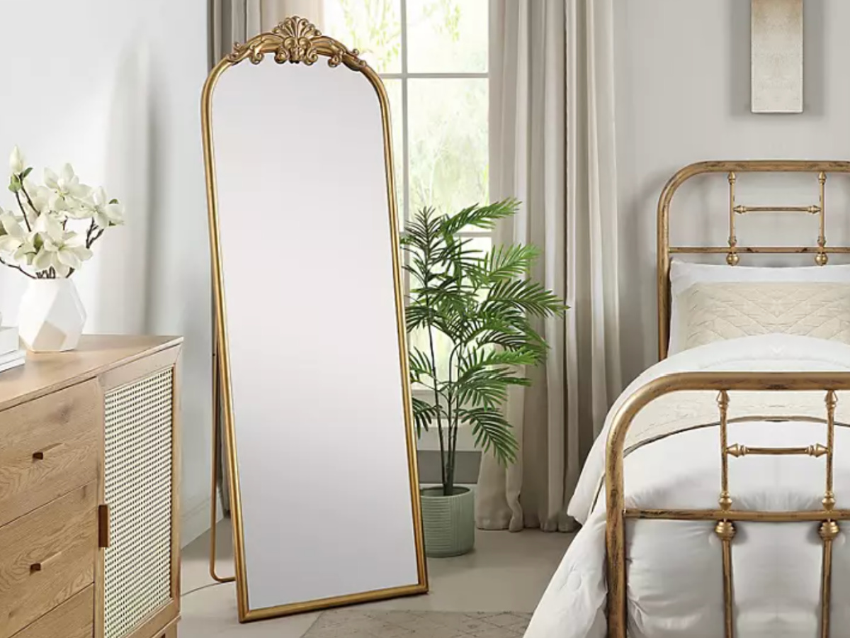 Gold floor mirror in bedroom next to gold framed bed