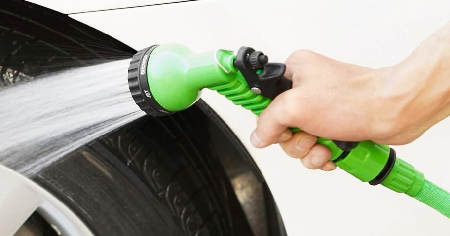 hand holding green garden hose nozzle pointed at car