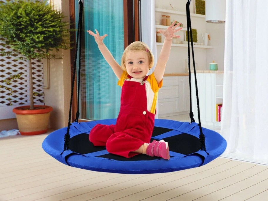 a little girl swinging on a blue saucer tree swing outdoors