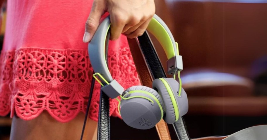 woman in a pink dress carrying a pair of grey and green headphones and a purse