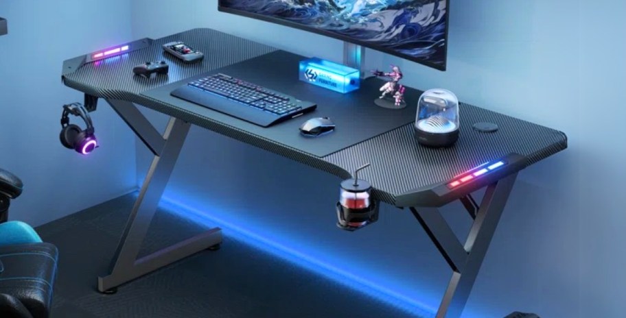 a black steel gaming desk with a monitor, keyboard, and mouse on top, it has colorful LED lights around it