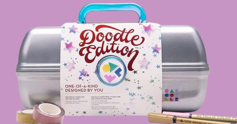 a silver Caboodles makeup case with a blue handle, has a white and colorful label around it that says "Doodle Edition" and markers and washi tape rolls in front of it