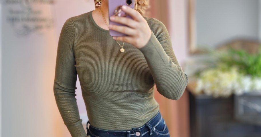 woman taking a selfie wearing a green ribbed bodysuit with jeans