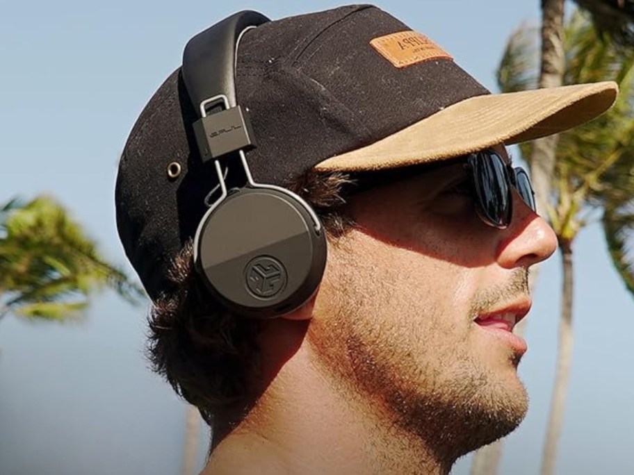 man wearing a pair of black JLab headphones with a black and tan hat and sunglasses