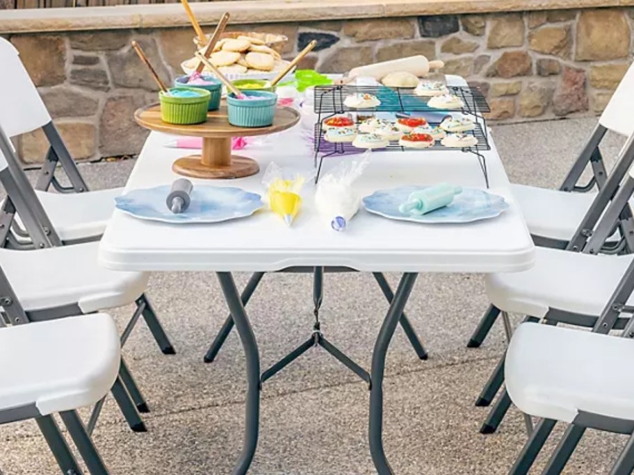 white folding table with plates and food on it, white folding chairs around it