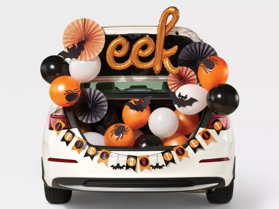 a white car with black, orange, white, and gold balloons and Halloween banners and decor