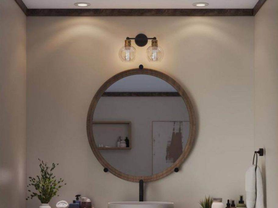 A bathroom with a single circular mirror with a vanity light hanging above it