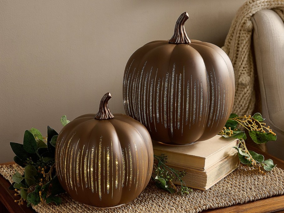 2 brownish orange decorative pumpkins with gold glitter accents on a table with fall decor