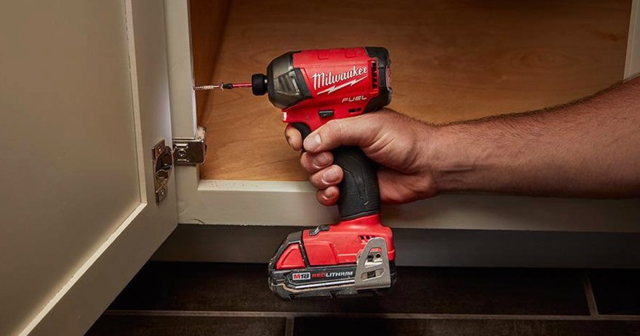 hand using a red Milwaukee Impact Driver on cabinet door