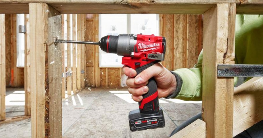 man using a Milwaukee drill and wood spade to cut hole in wood