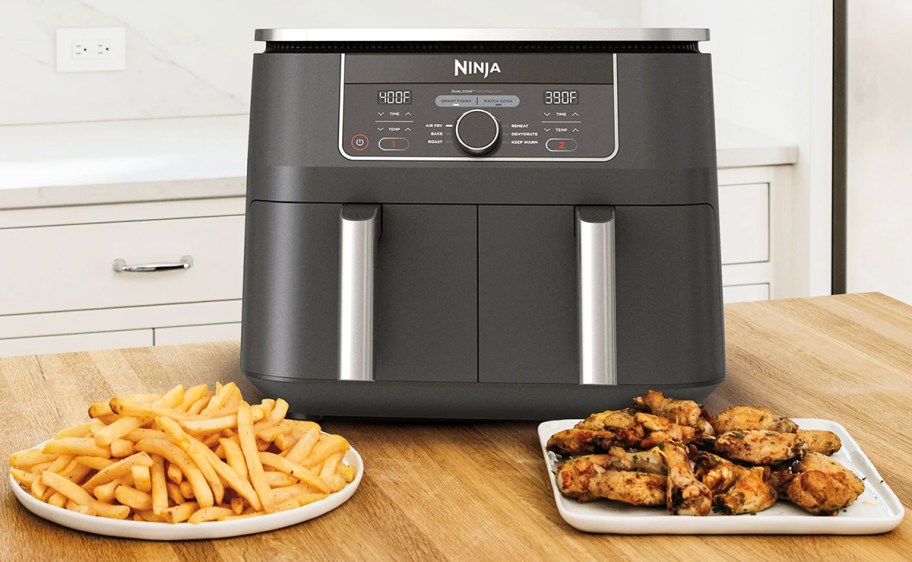 Ninja Foodi Dual Air Fryer next to a plate of fries and chicken wings