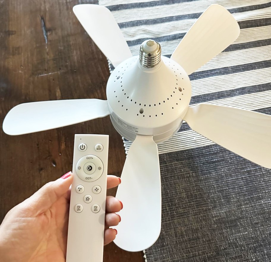 hand holding a remote in front of a white socket ceiling fan