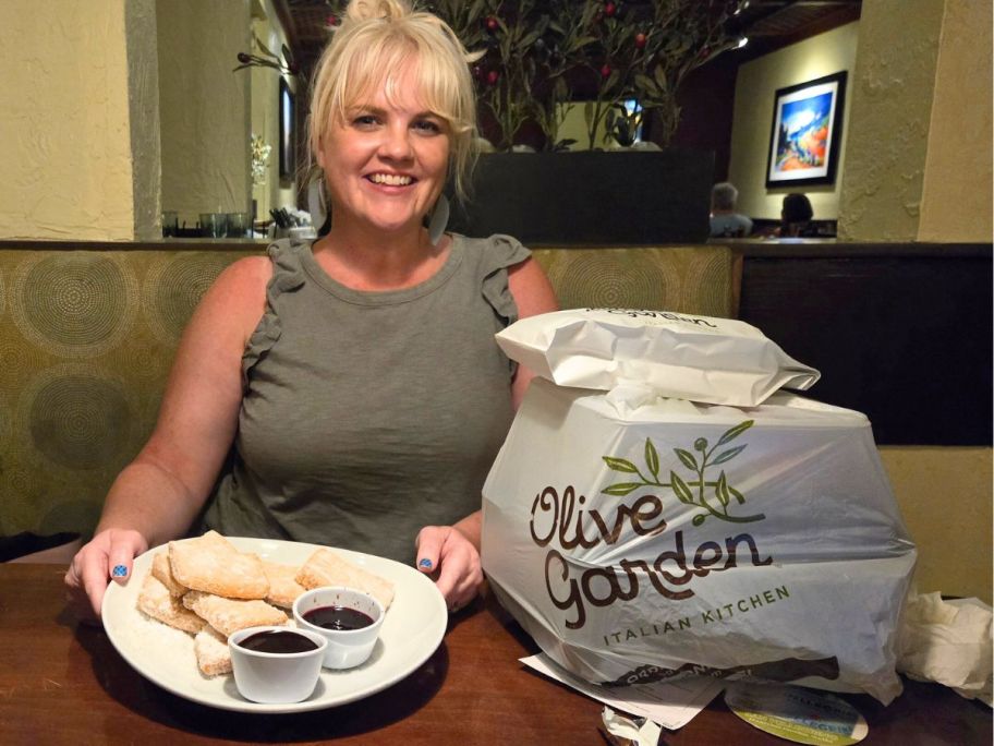 Woman with a dessert in front of her and a huge stack of takeout food in bags