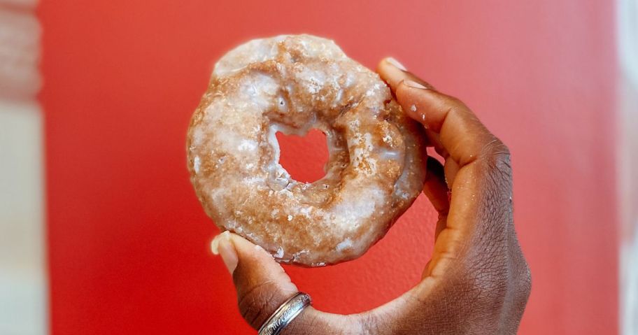 Hand holding up a Pumpkin Spice Cake Doughnut from Krispy Kreme